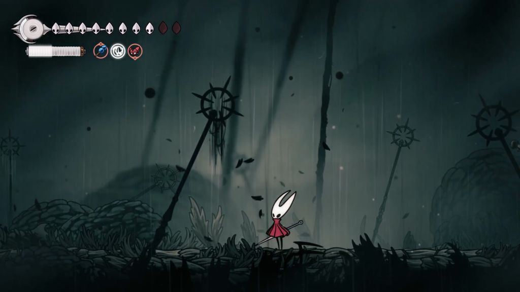 The ground is littered with grey-blue feathers and tall religious stakes while the sky rains. The sky is primarily grey.